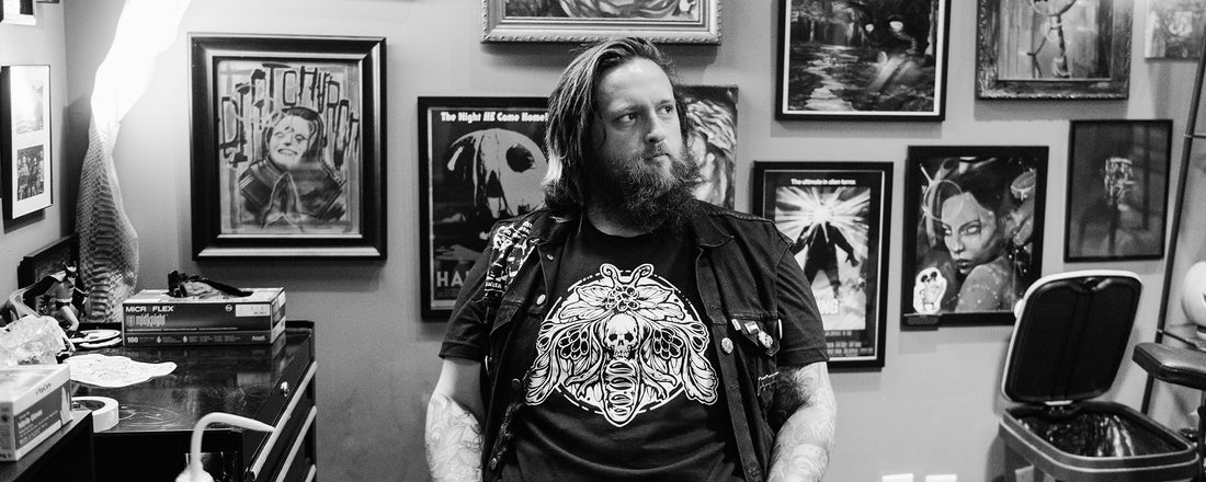 A tattoo artist in his tattoo shop wearing his own Death Moth tattoo design on a t-shirt.