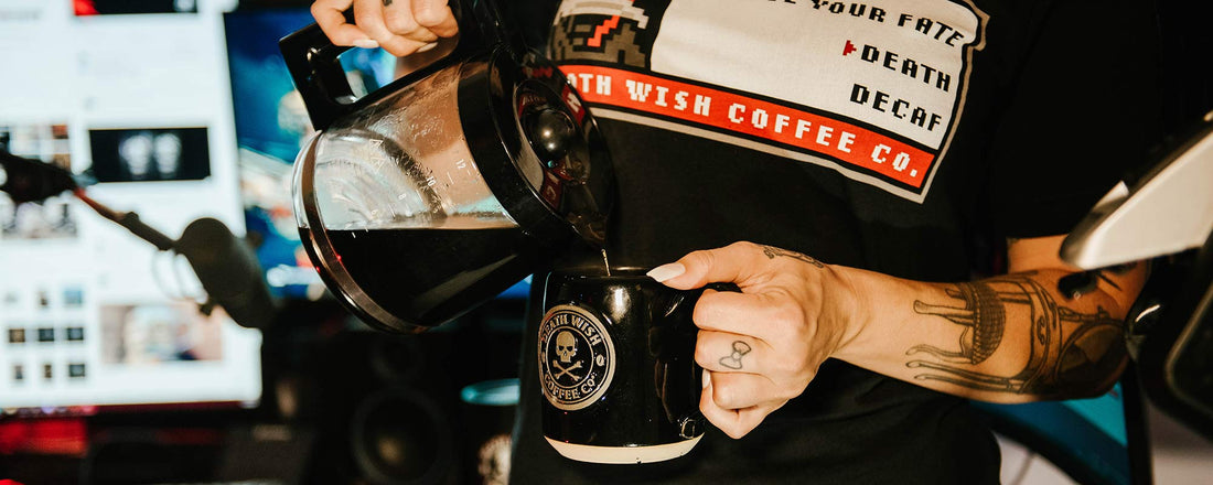 A pot of coffee being poured into a black mug.