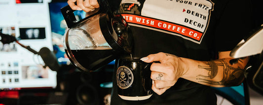 A pot of coffee being poured into a black mug.