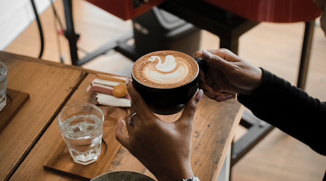 A woman holding a coffee mug with almond milk foam on top.