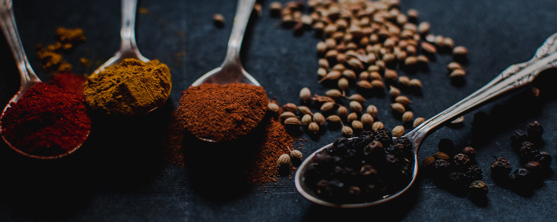 A black table with four spoons full of various spices. Photo Credit: Pratiksha Mohanty via Unsplash.