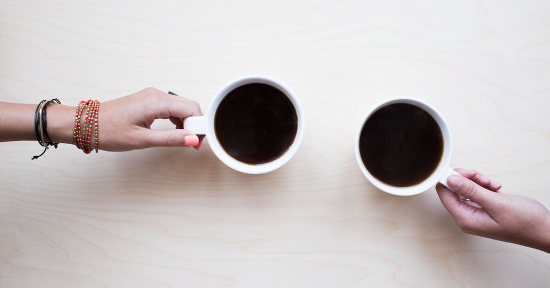 Two friends holding their cups of coffee next to each other.