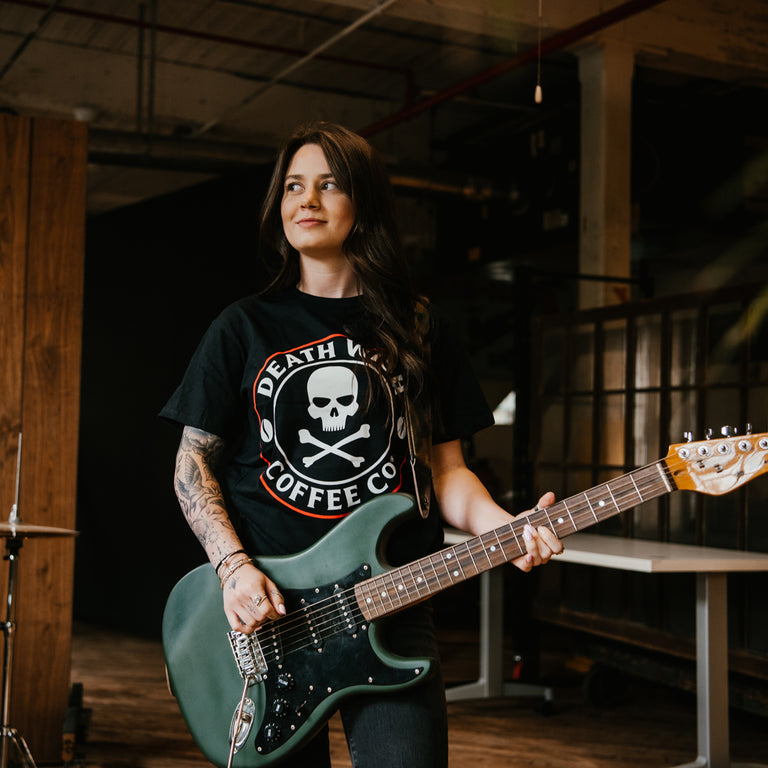 A girl playing guitar in the Death Wish Coffee Core Classic Logo Tee.