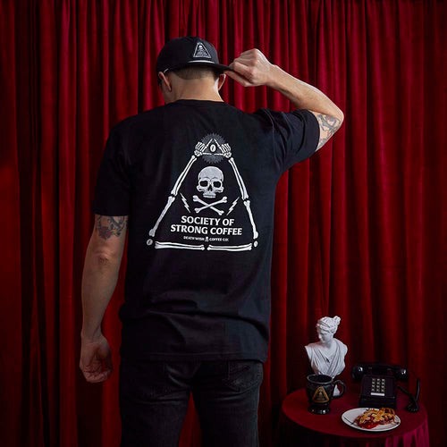 A male model wearing the Death Wish Coffee Society of Strong Coffee Insignia Tee and Hat.