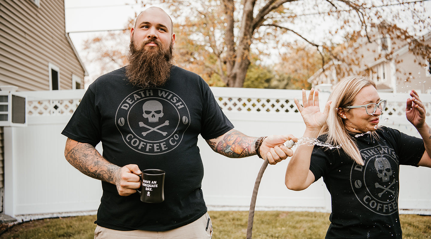 A man spraying a girl with a hose while both wearing the Shadow Logo T-Shirt.