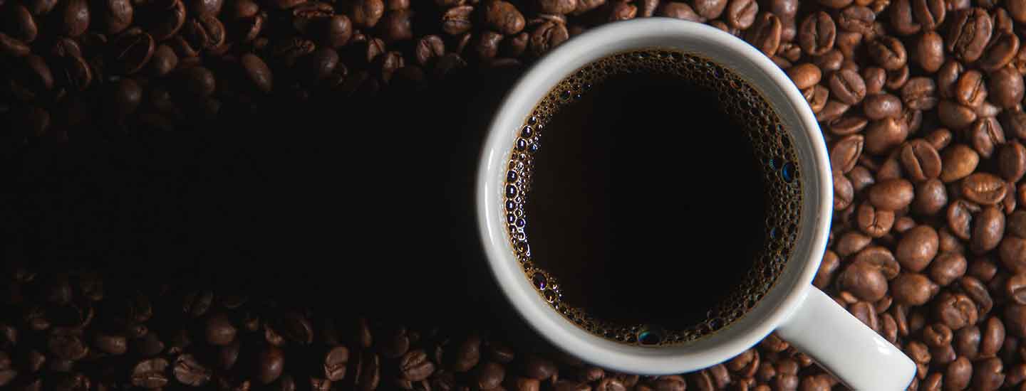 A mug of coffee surrounded by coffee beans.