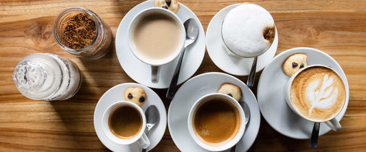 Various cups of coffee on a wooden table.