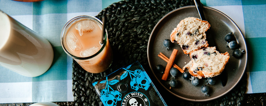 A breakfast table with a bag of Blueberry coffee, iced coffee and blueberry coffee cake.