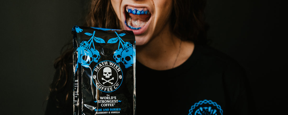 A woman holding a bag of Death Wish Blue and Buried Coffee with blue teeth.