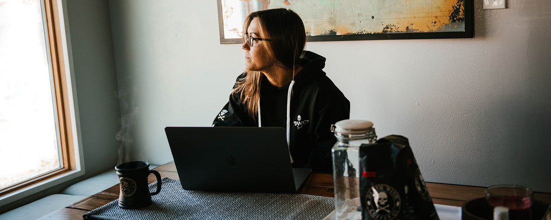 A woman working on her computer with coffee and gazing out the window.