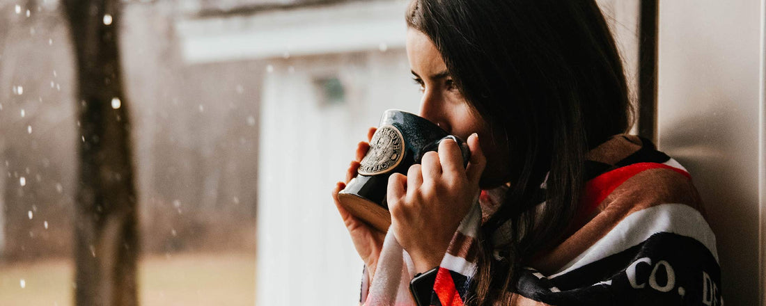 A female wrapped in a blanket sipping coffee out of a Death Wish Coffee mug 