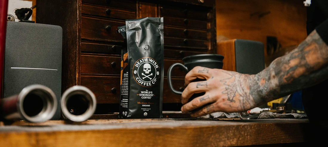 A man with a sleeve of tattoos reaching for a mug of medium roast coffee.