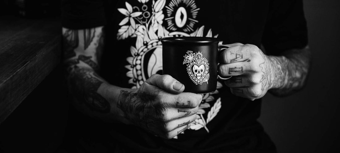 A man with tattoos with tattoos on his arms holding a mug of Death Wish Coffee.