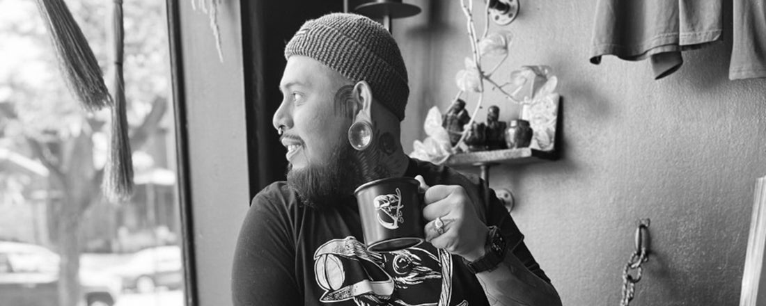 Tattoo artist, Emmanuel Mendoza drinking coffee out of a black mug in his tattoo shop.