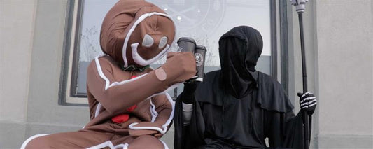 A Gingerbread man cheersing the Grim Reaper with a cup of Death Wish Coffee.