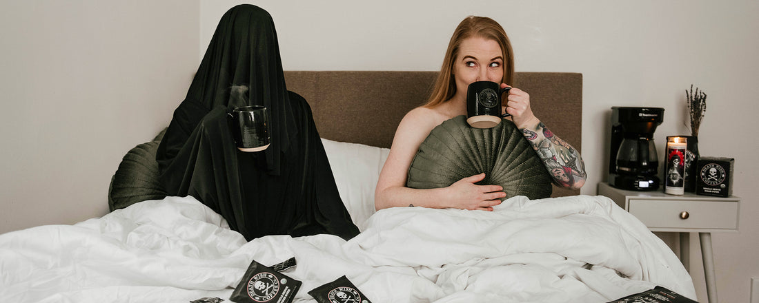 Grim Reaper in bed with a woman drinking coffee in bed.