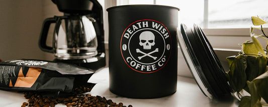 A white kitchen countertop with a large kilo coffee storage container sitting next to a coffee maker.