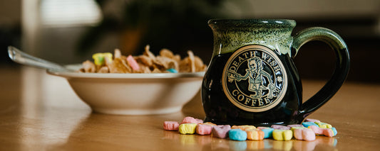 A mug with a Lucky Larry medallion sitting on a table next to a bowl of Lucky Charms.