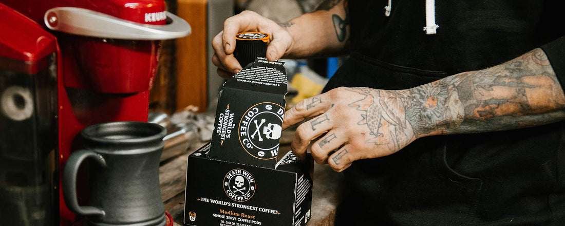 A red Kuerig with a black mug and a man with a tattooed arm reaching into a box of Medium Roast K-Cups.