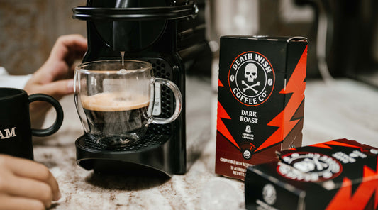 A black and red box of Dark Roast espresso capsules next to a coffee brewer
