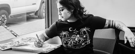 A woman with tattoos sketching a tattoo design at her tattoo shop.