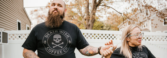 A man drinking coffee and spraying his friend with a hose in the Death Wish Coffee Shadow Logo Tee.