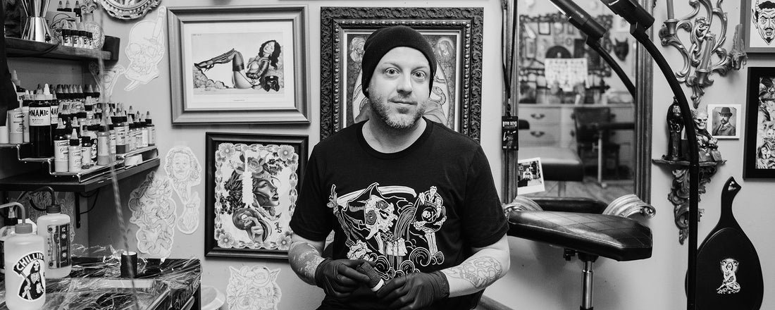 A man wearing a black and white Reaper tee in a tattoo shop.