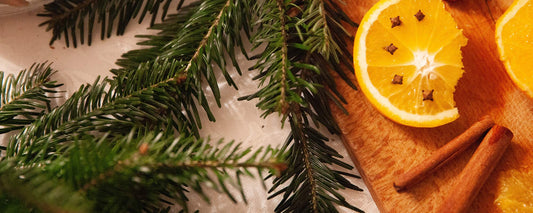 An aerial view of a counter with evergreen branches, oranges and cinnamon. Image Credit: Alicja Gancarz via Unsplash.