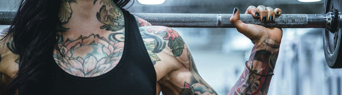 A woman with tattoos lifting a bar with weights in a home gym.