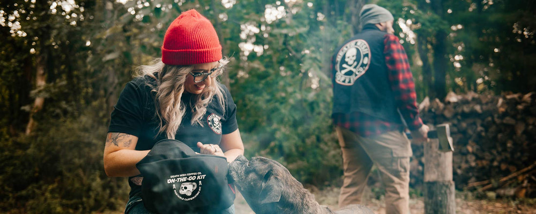 A female sitting next to a fire with a dog and a male in the background.