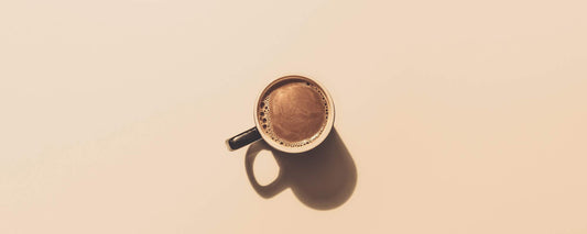 An aerial image of a mug of butter coffee on a tan background.
