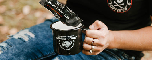 A woman outside pouring Death Wish Instant Coffee into a black mug.