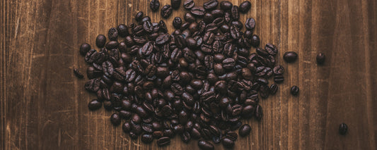 Coffee beans scattered across a wooden stained table. Photo credit: Joris Molenaar via Unsplash.