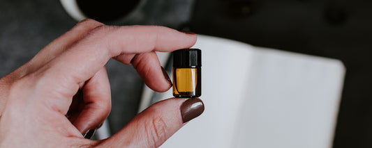A woman with painted nails holding a small bottle of coffee essential oil. Photo Credit: Kelly Sikkema via Unsplash.