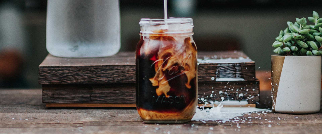 A mug mason jar of keto coffee with almond milk being poured from above.