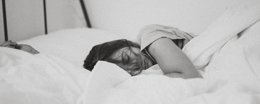 A woman sleeping in bed with white bedding. Photo Credit: Kinga Cichewicz via Unsplash.