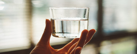 A woman's hand holding a glass of water in front of a window. Photo Credit: Manki Kim via Unsplash.