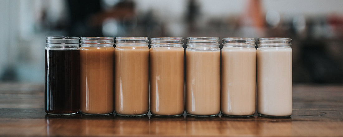 A countertop with mason jars filled with different shades of coffee from black coffee to coffee with creamer. Photo credit: Nathan Dumlao via Unsplash.