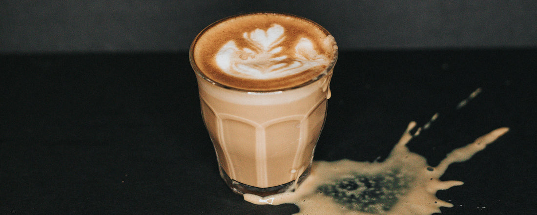 A cup of coffee spilling onto a black countertop and leaving a coffee stain. Photo Credit: Nathan Dumlao via Unsplash.