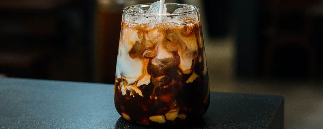 A glass with ice cubes and cold brew coffee with creamer being poured in. Photo Credit: Pariwat Pannium via Unsplash.