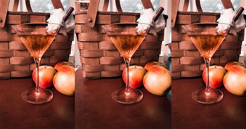 An image of three pumpking spiced martinis with a fall background featuring a basket and apples.