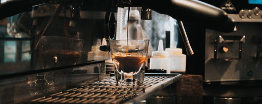 A shot of espresso in a clear shot glass under an espresso machine. Photo Credit: Tyler Nix via Unsplash.