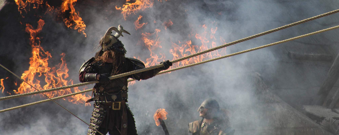 A Viking with a large spear standing proudly in front of a fiery burned down city.