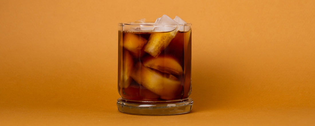 A glass filled with ice cubes and coffee soda on an orange background. Photo Credit: Wade Austin Ellis via Unsplash.