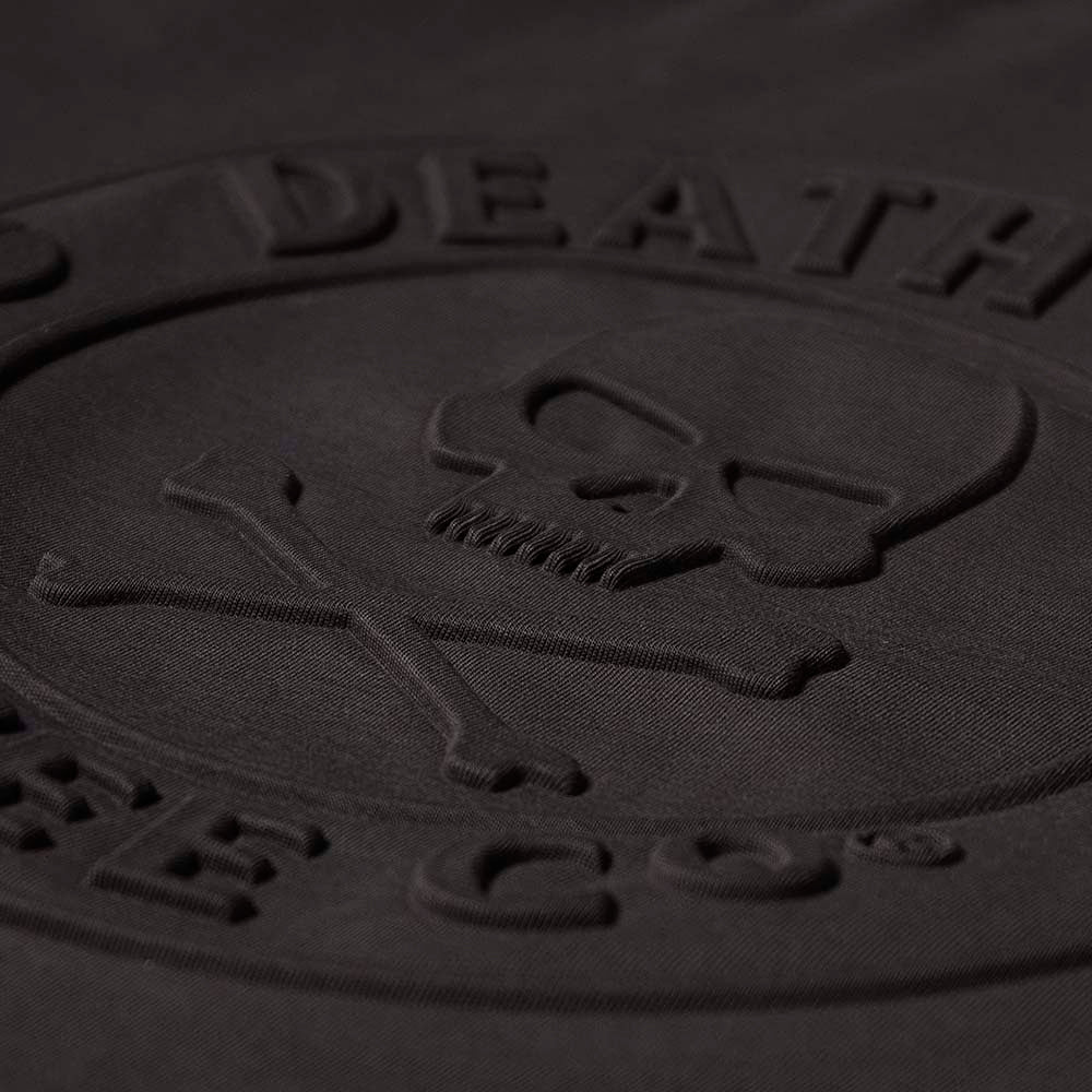 Close-up of a black embossed logo with a skull and crossbones design on the Death Wish Coffee Erebus Embossed Tee.