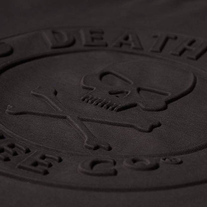 Close-up of a black embossed logo with a skull and crossbones design on the Death Wish Coffee Erebus Embossed Tee.