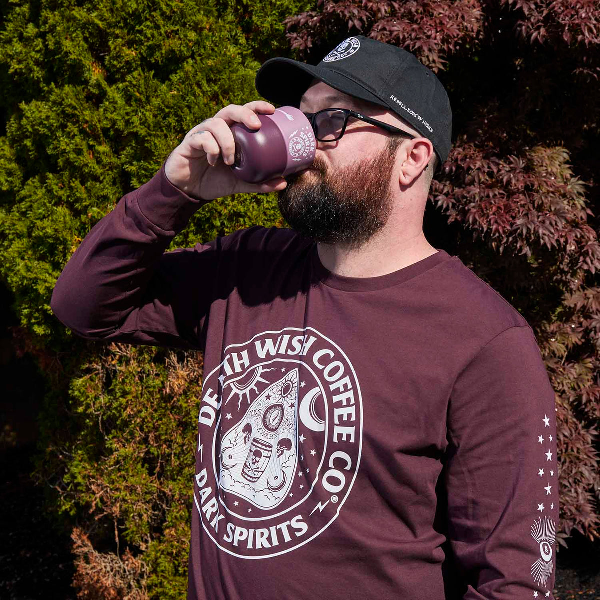 A model wearing the Death Wish Coffee Dark Spirits Long Sleeve and drinking from the matching Klean Kanteen.