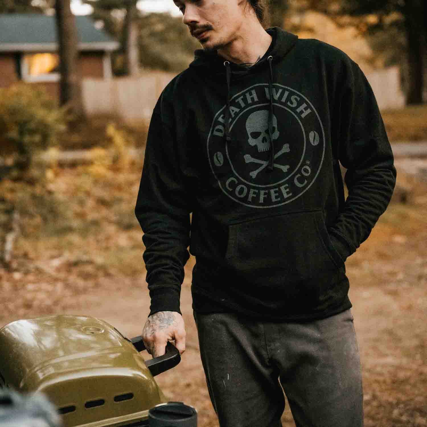 Cooking on a portable grill wearing the Death Wish Coffee Shadow Logo Hoodie.