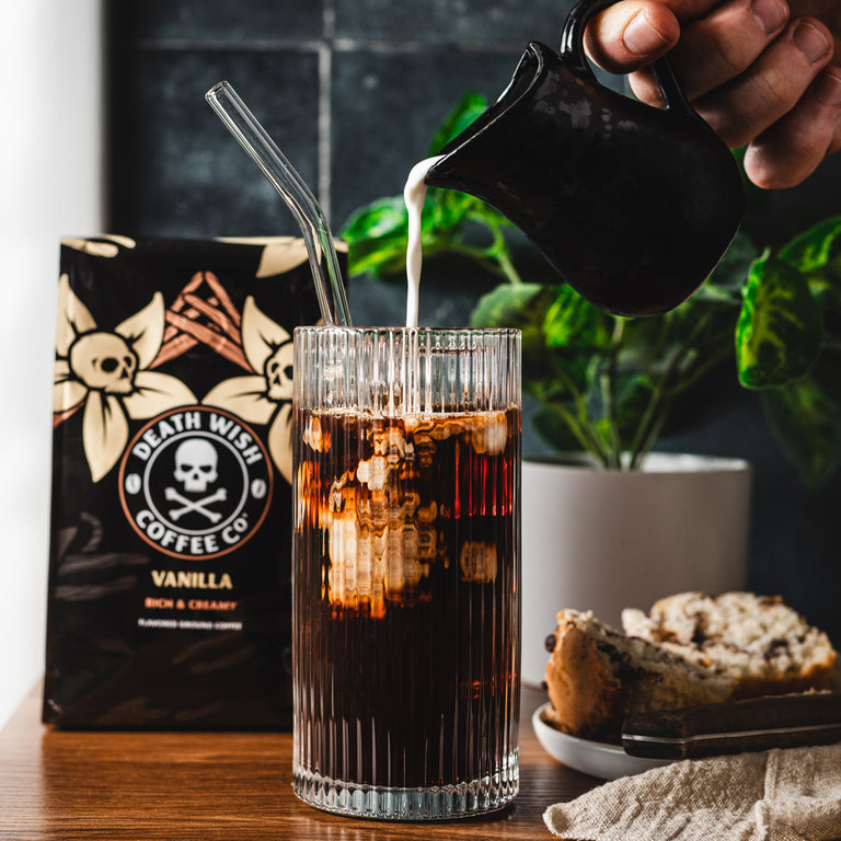 Pouring creamer into a cup of iced vanilla coffee.